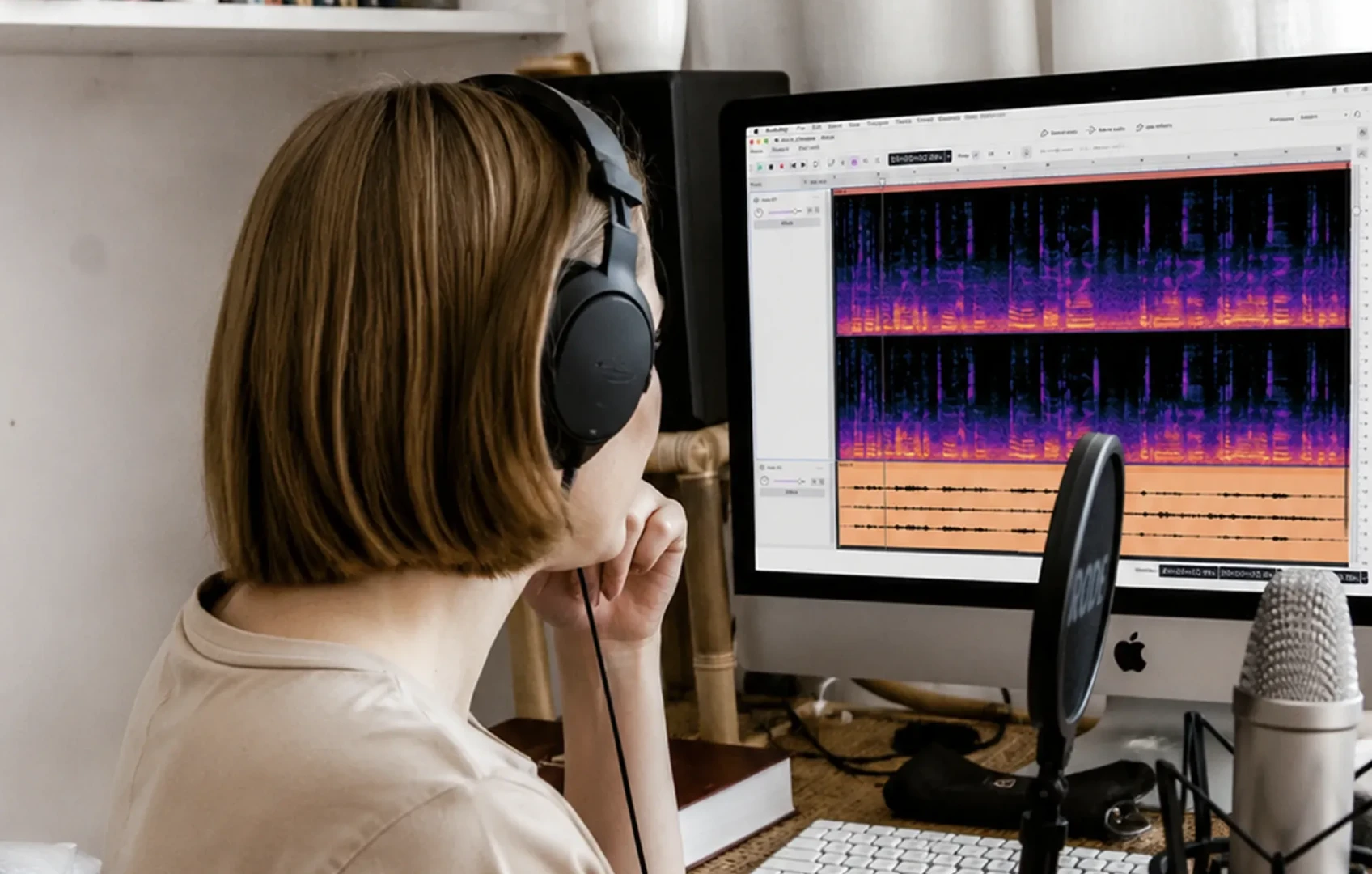 Person wearing headphones working with Audacity 4 on a desktop computer beside a microphone in a home recording setup.