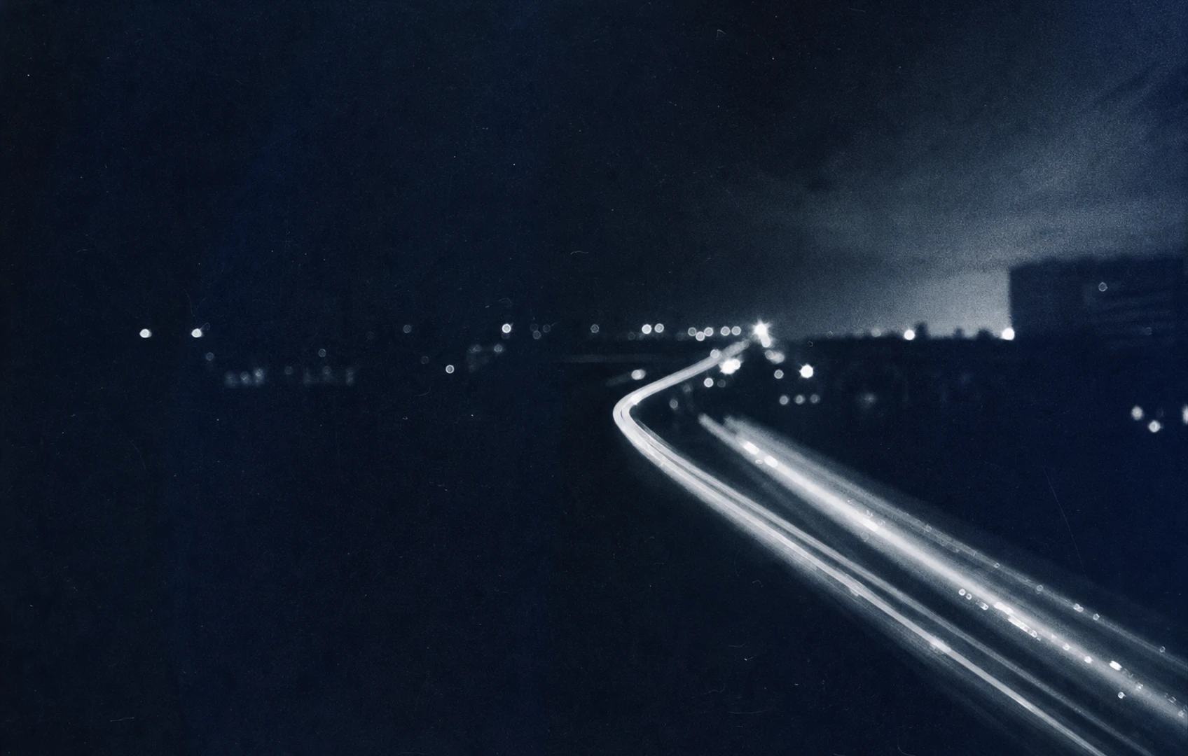 A grainy editorial collage of twilight blue paper textures, soft geometric speaker-like shapes, blurred city lights, and scattered cutout stars suggesting distance and suspended motion
