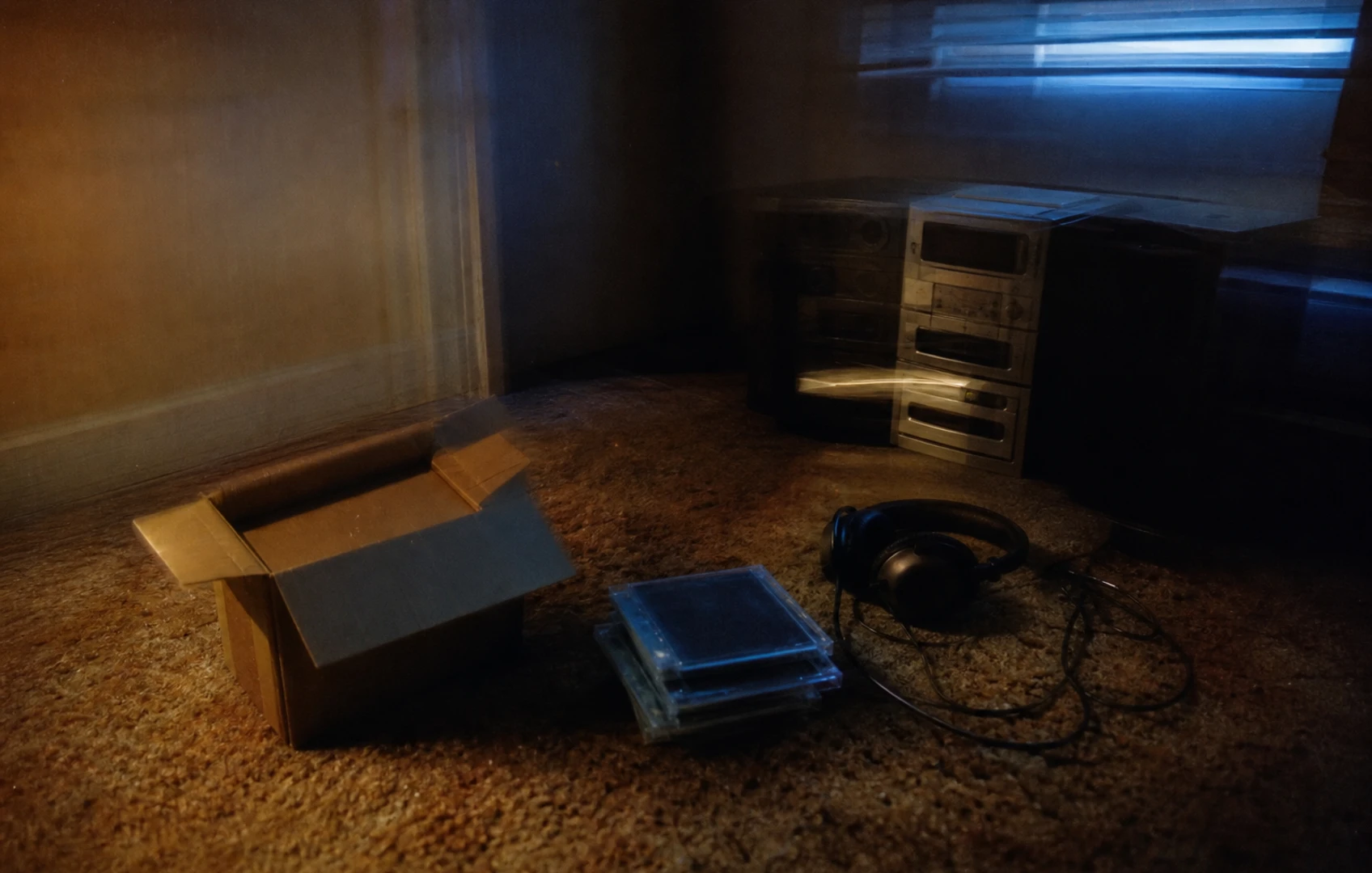 Grainy, flash-lit still life of blank jewel cases, coiled headphones, and an open cardboard mailer on worn carpet.