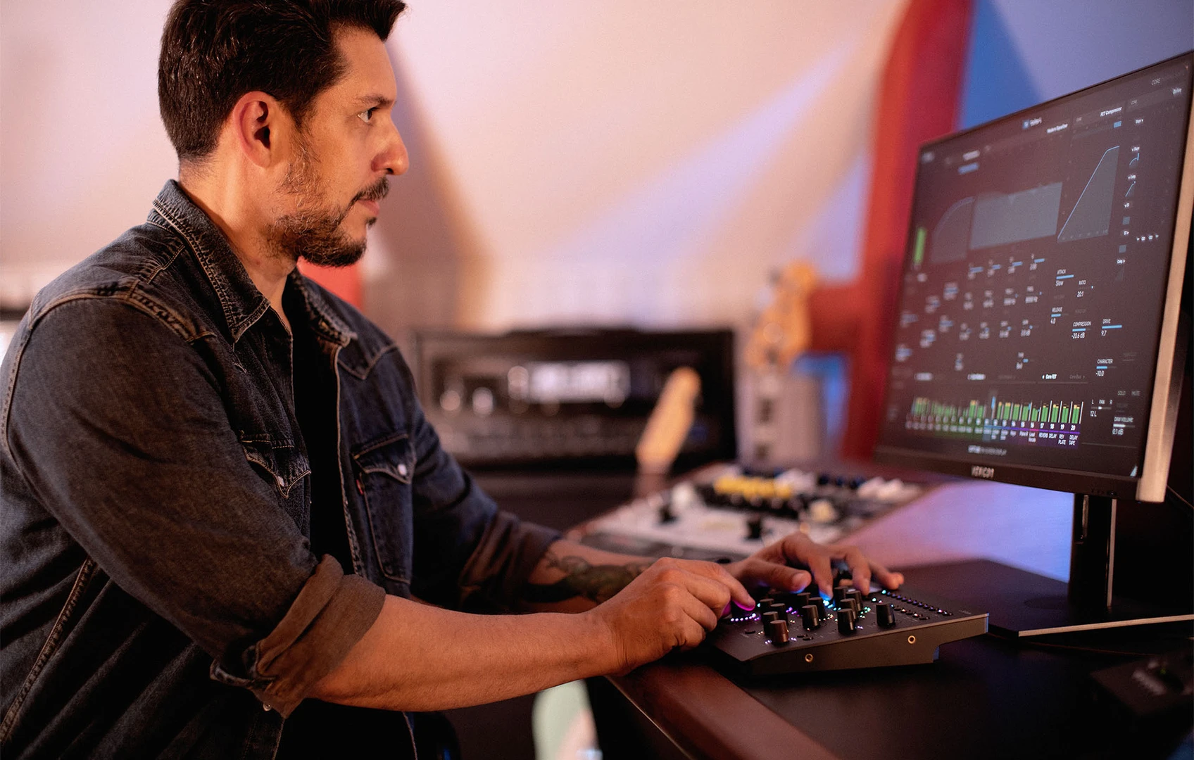 A musician uses the Softube Console 1 Compact control surface beside a computer monitor in a studio